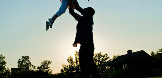 Sunset silhouette of dad throwing daughter up in the air.