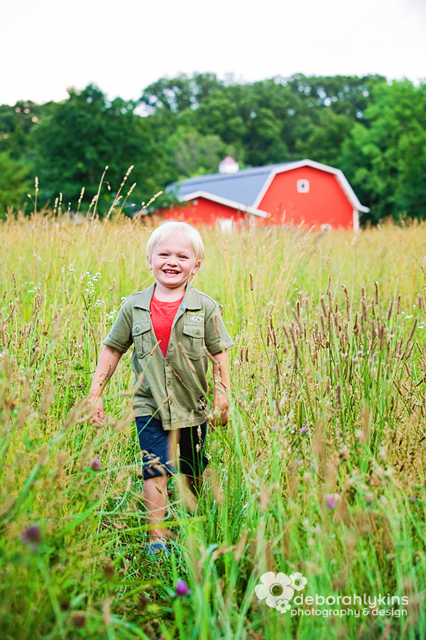Child portrait in tall grass with red barn.